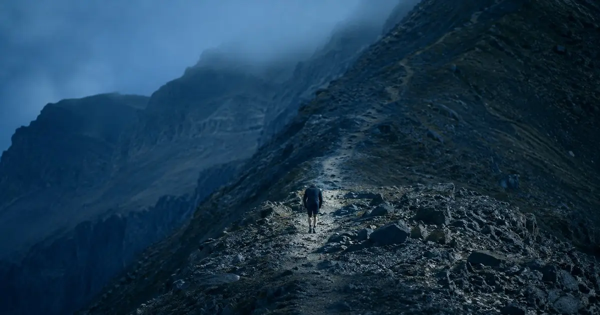 Lone runner on a mountain ridge trail in blue dusk light and mist