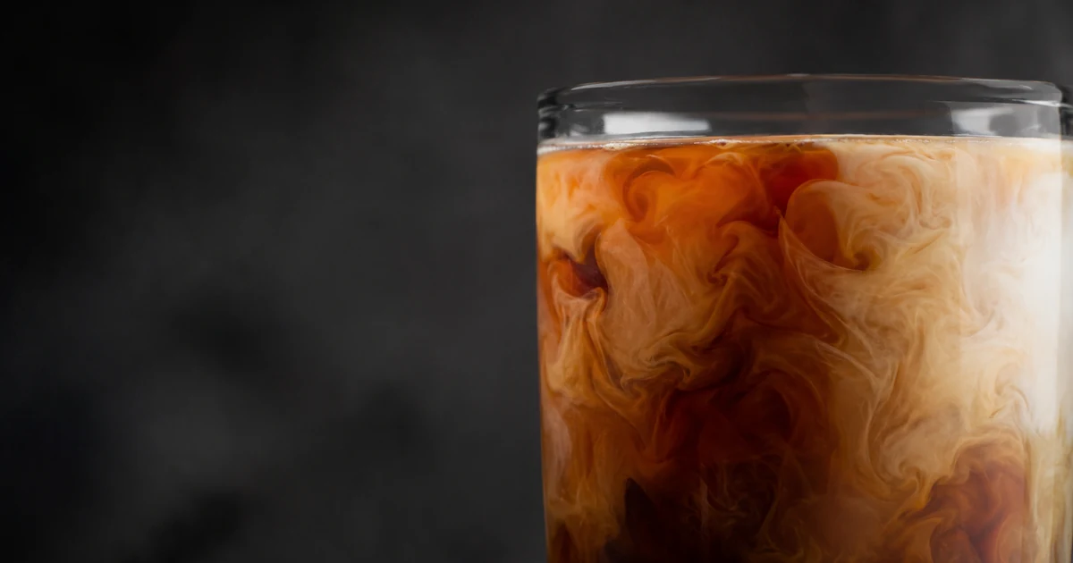 Close-up of a glass of coffee with freshly poured milk swirling through it, the two liquids still blending